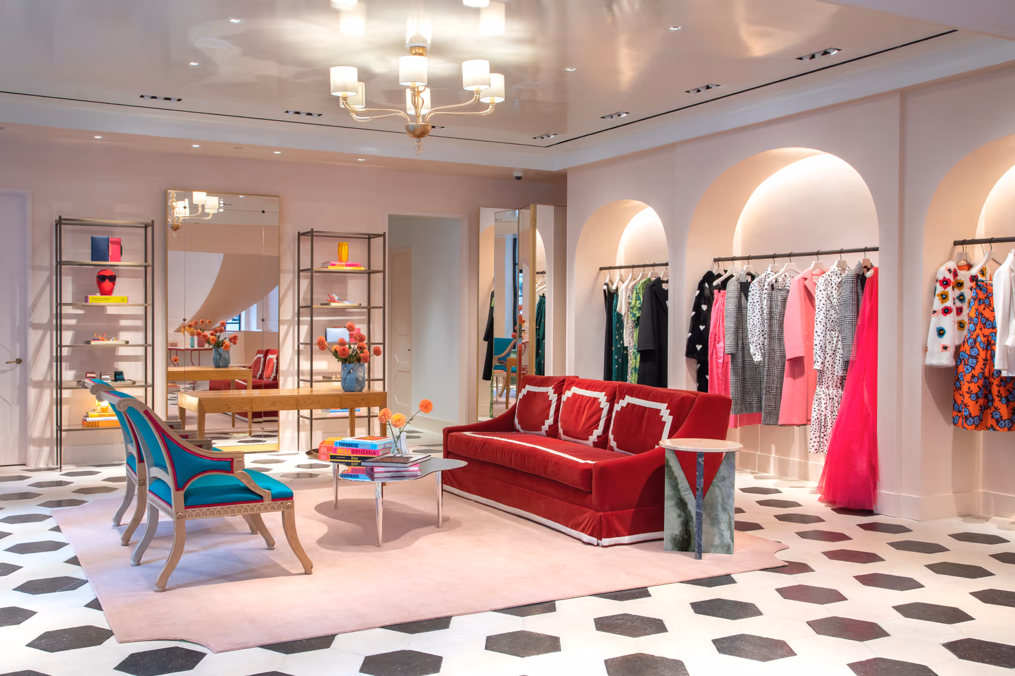Elegant boutique interior with a red velvet sofa, turquoise chairs, a mirrored wall, and clothing displayed in arched niches.